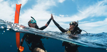 Two divers at the surface high fiving, with an inflated surface market buoy