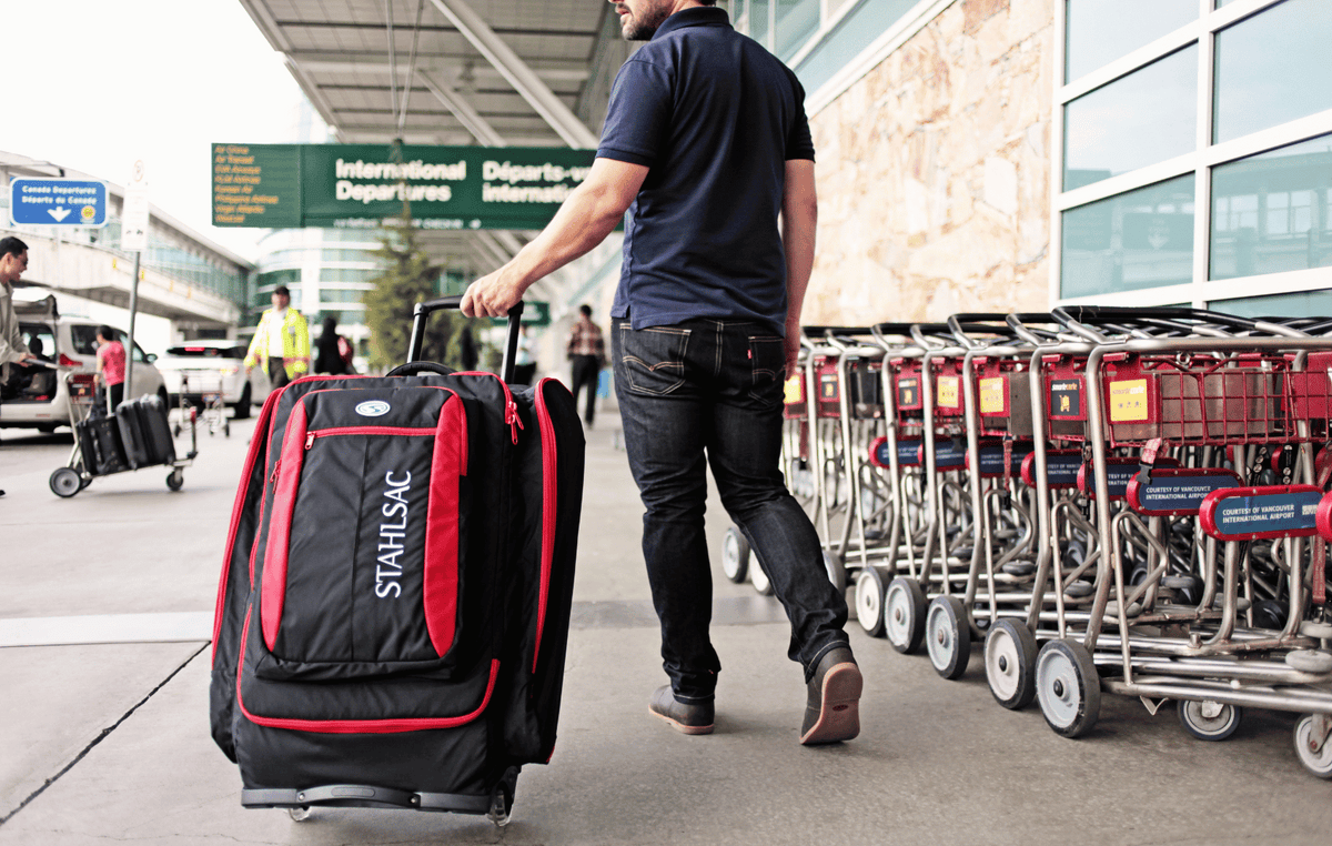 A man is walking at the airport with a suitcase of dive gear