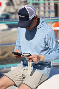 Diver holding an Oceanic O.i Wrist and iPhone while seated by a boat.